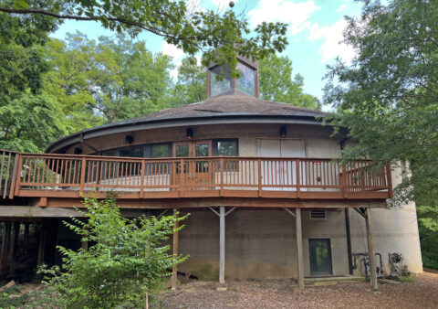 Brown circular building with a raised walkway surrounded by trees.